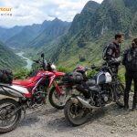 two people standing next to motorcycles on a rocky hill