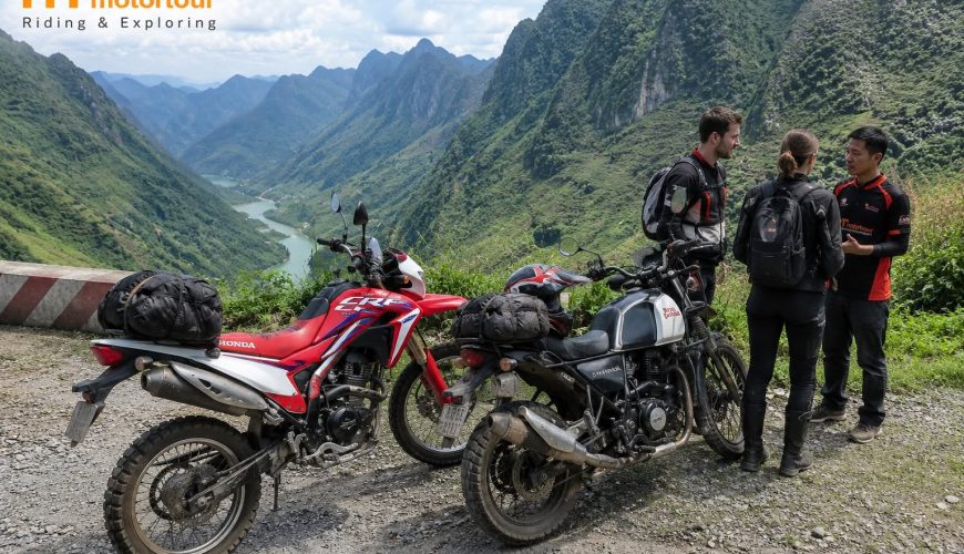 two people standing next to motorcycles on a rocky hill